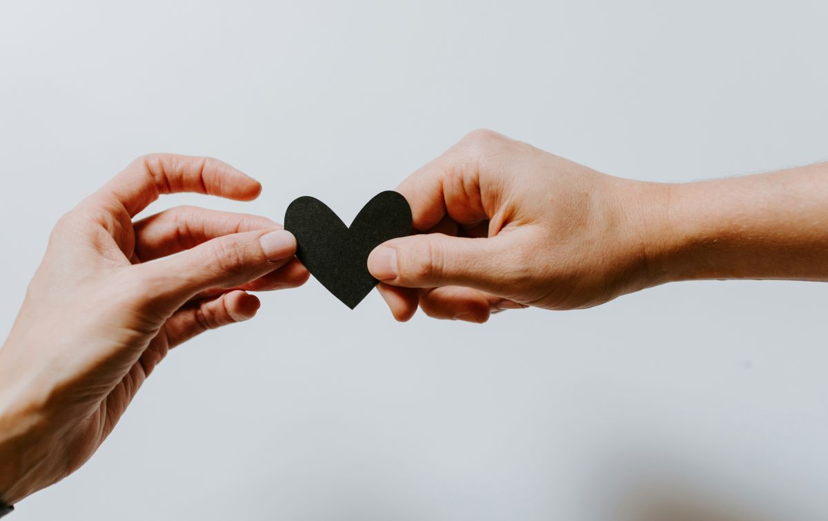 Two hands passing a paper heart — Valor to Virtue, giving back