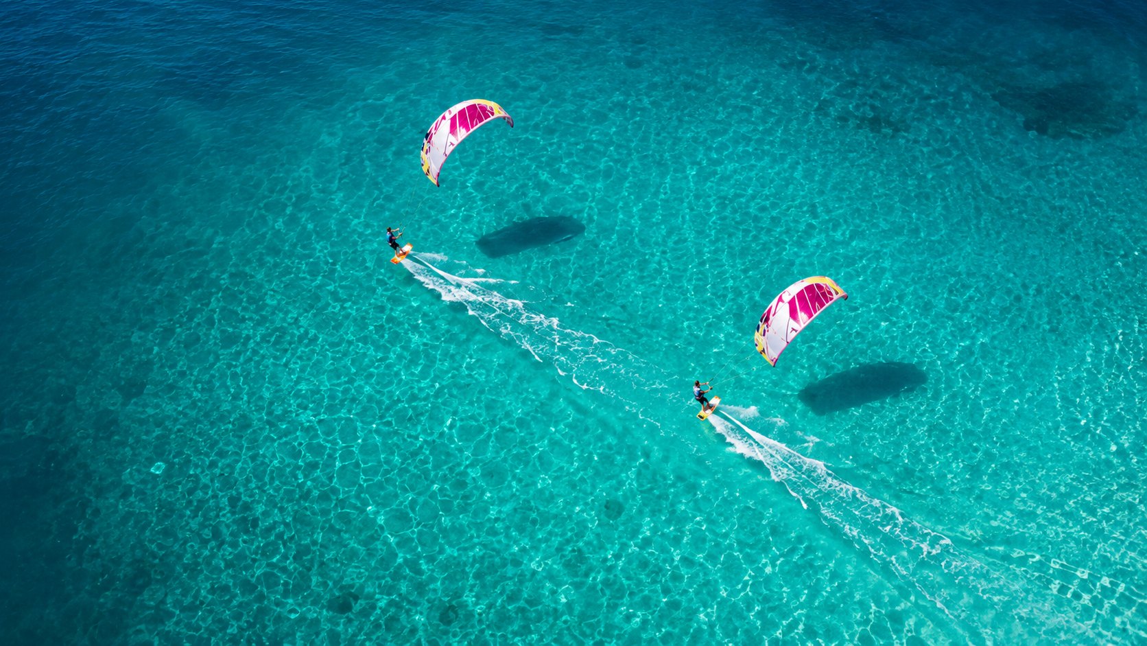 Aerial view of two kitesurfers riding across clear turquoise water off Watamu
