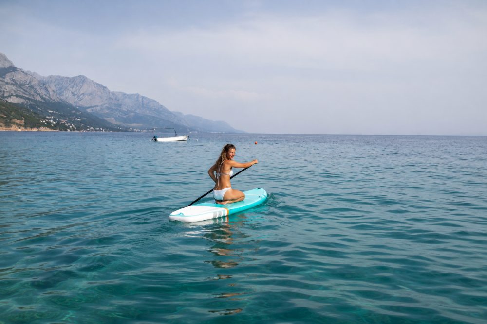 Paddler kneeling on a stand-up paddleboard on calm blue sea