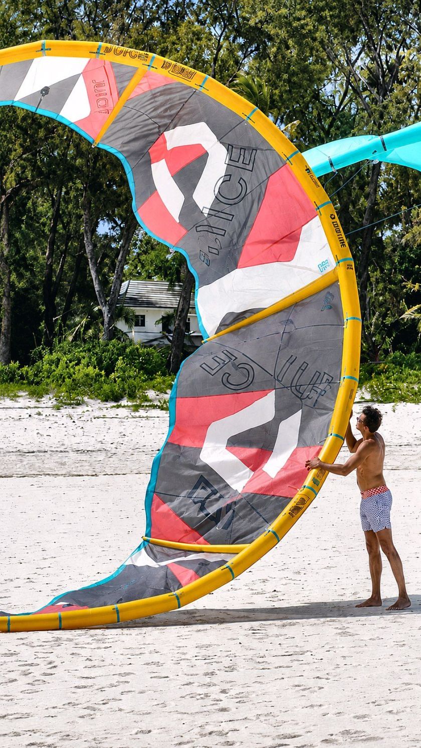 Rider holding an inflated kite ready to launch on a white-sand beach