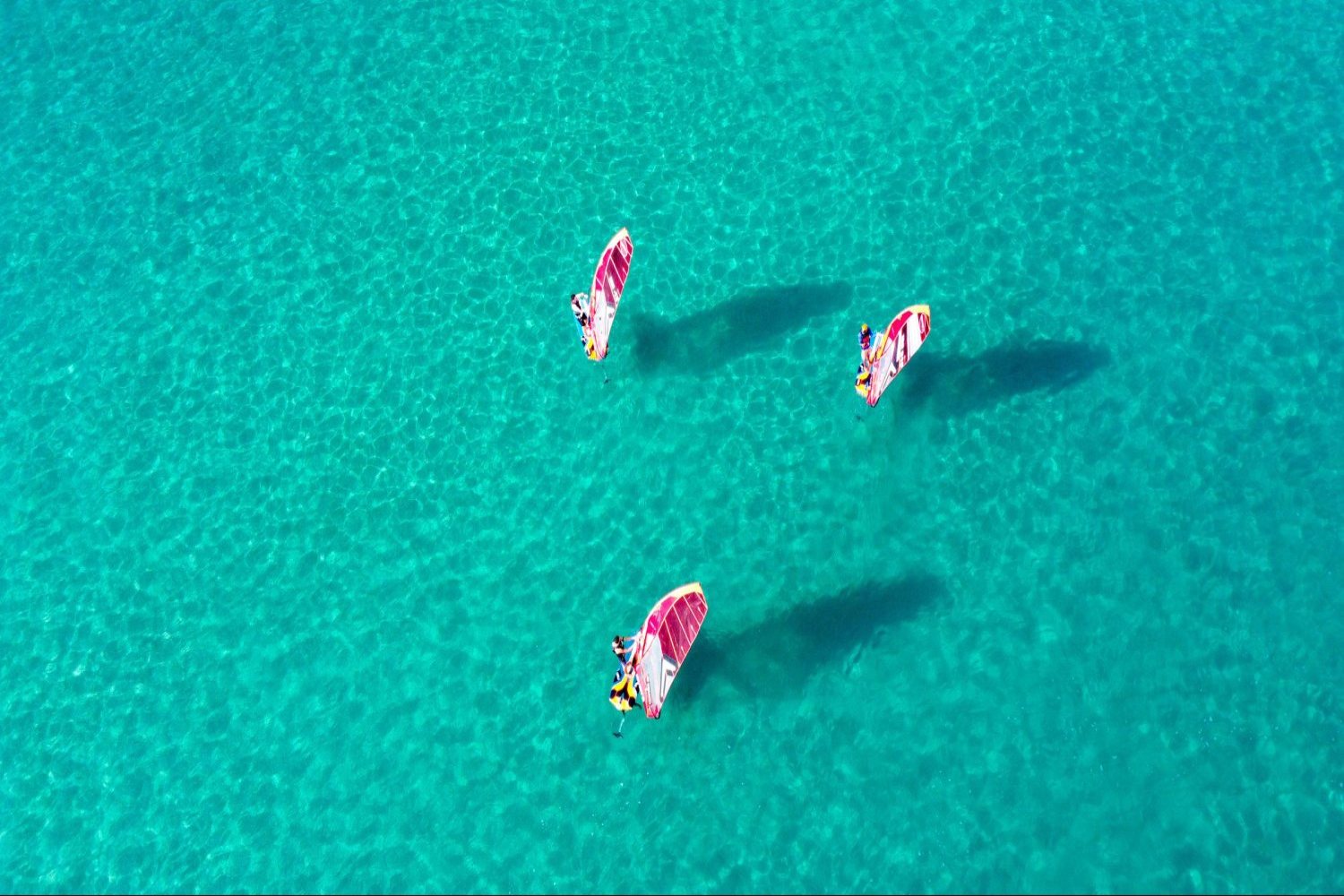 Aerial view of flat turquoise water with riders
