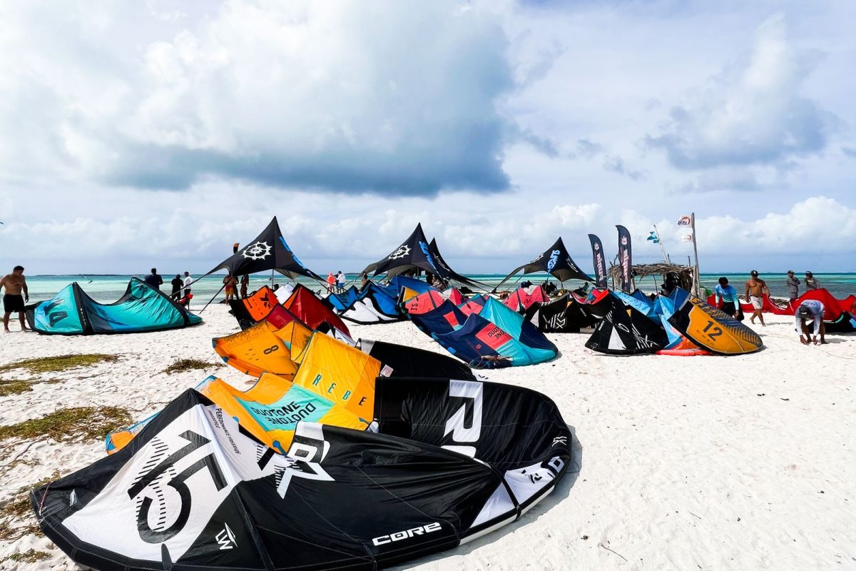 Kites and boards laid out on a white-sand beach, ready to rig