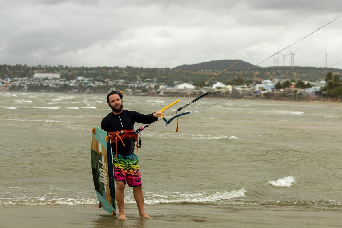 Kitesurfer in harness on the beach with board and bar in hand