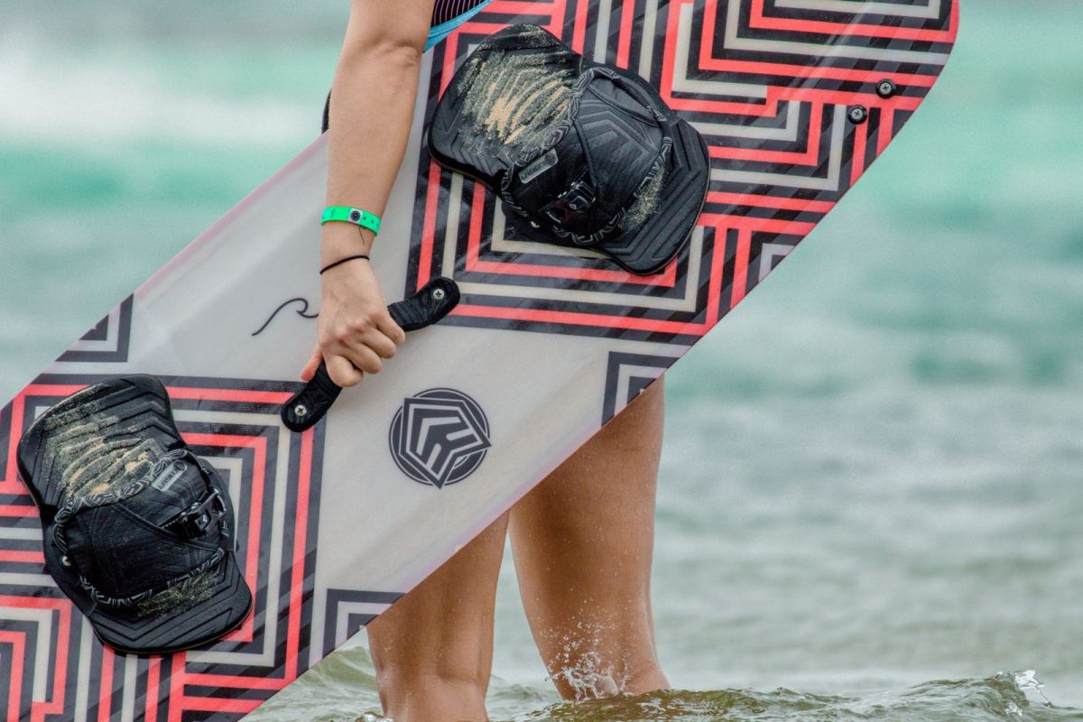Close-up of a twin-tip kiteboard with foot straps carried through shallow water