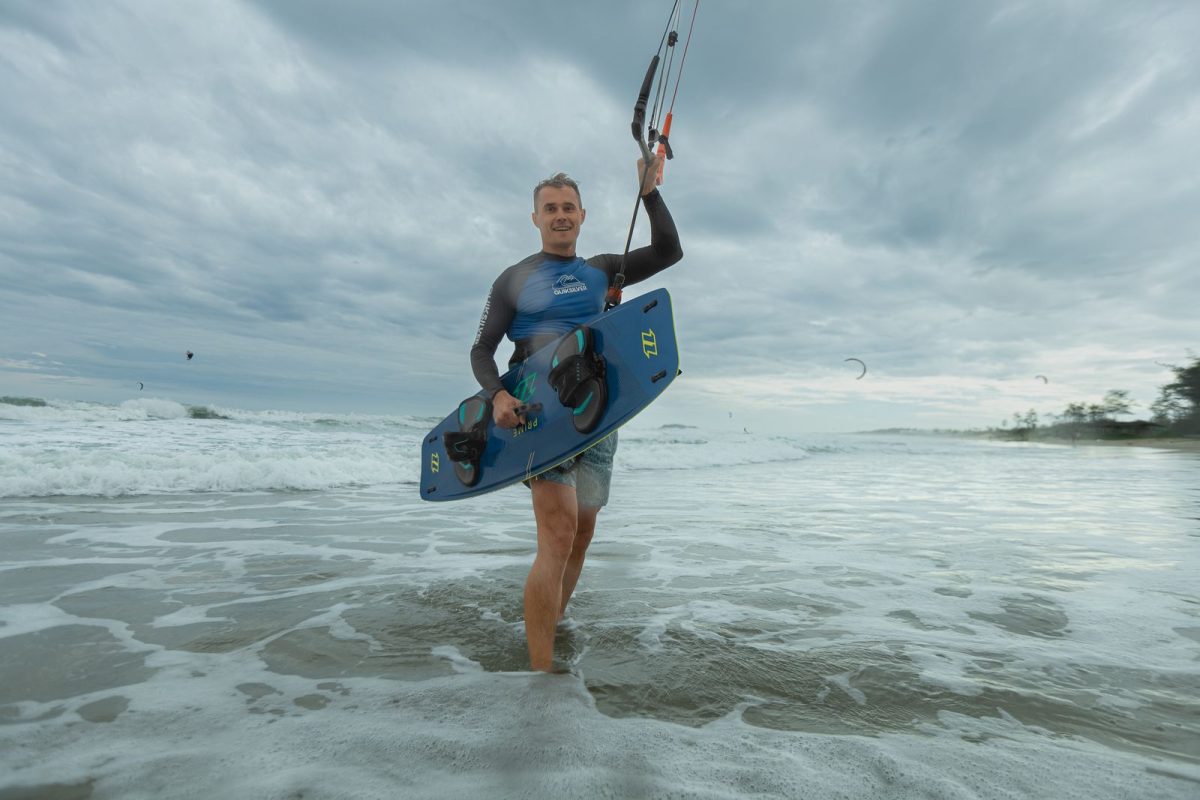 Kitesurfer walking out of the shore break carrying a twin-tip board