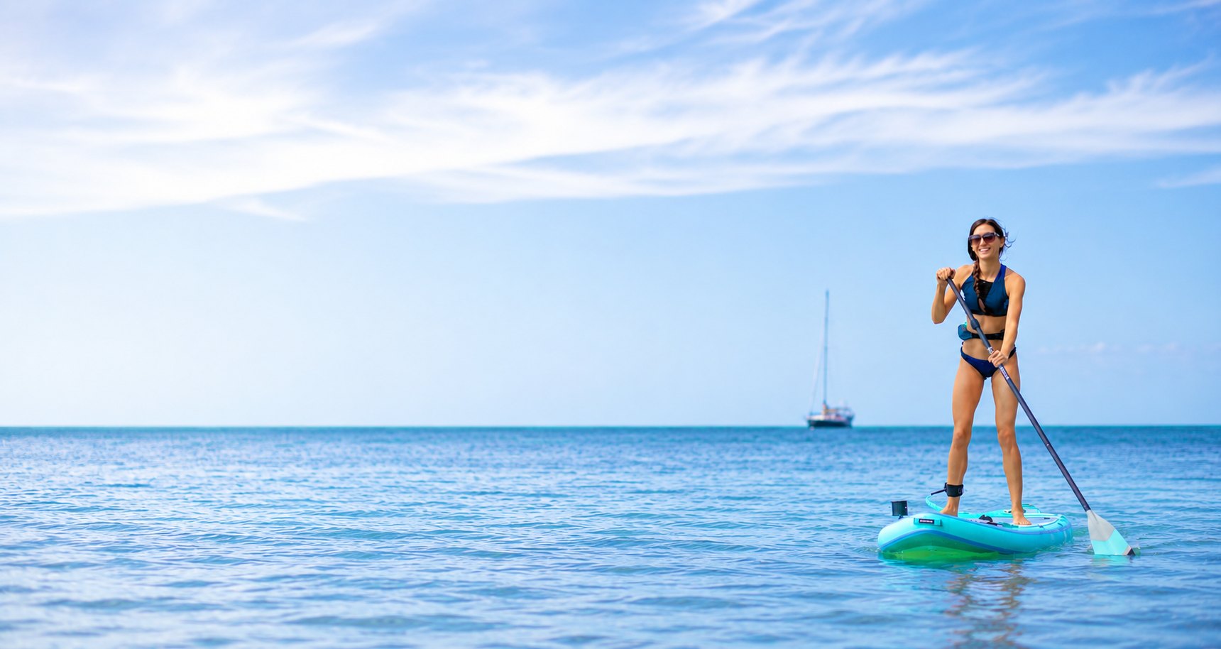 A paddler crossing flat blue water on a stand-up paddleboard